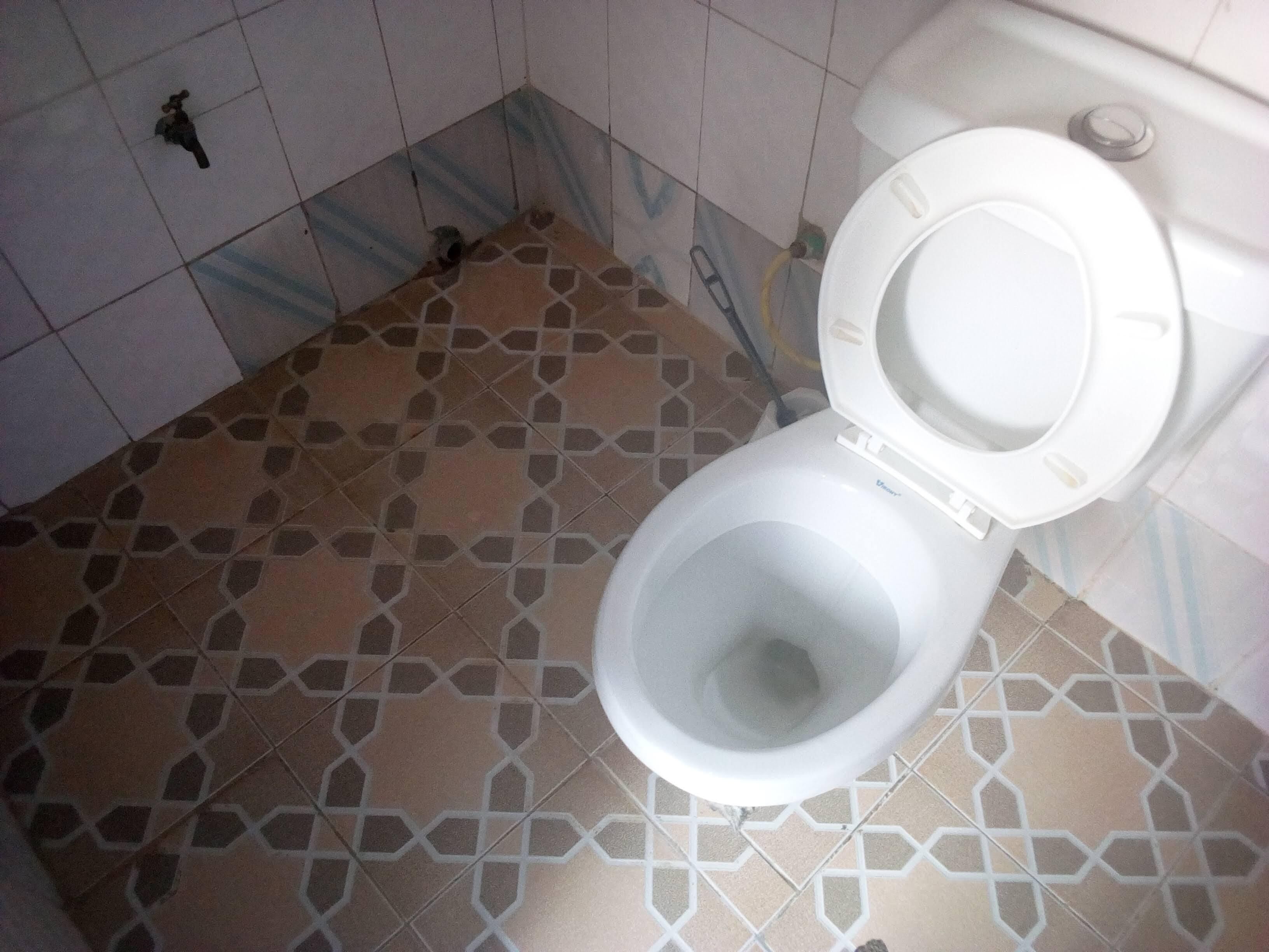 A toilet with a white seat and lid, a patterned floor, and a wall-mounted flush handle.