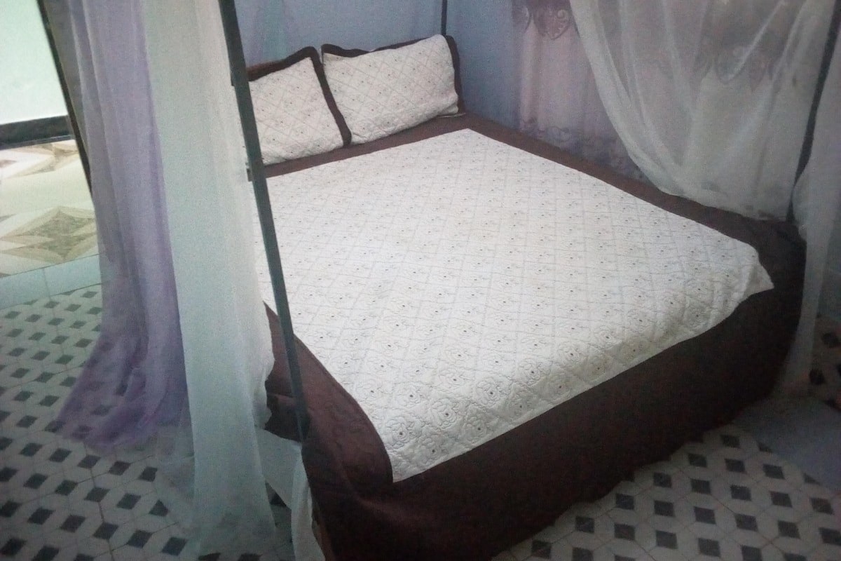 A bed with a quilted cover, a headboard, and a curtain.