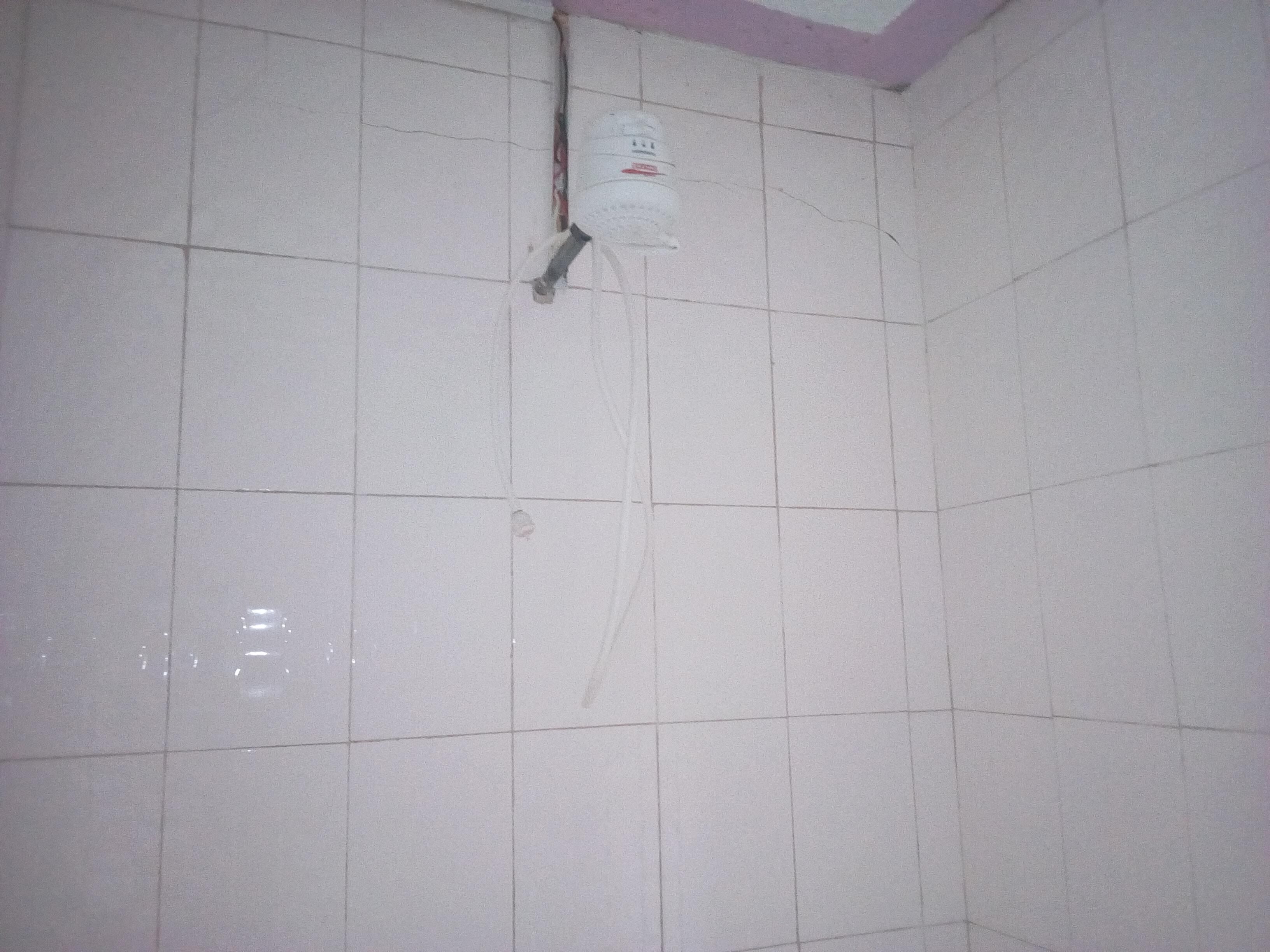 Un baño con baldosas, una tubería a la vista y un accesorio de iluminación en la pared.