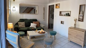A modern living room with a green sofa, a white coffee table, and a blue armchair. There is a staircase leading to another level, a small wooden cabinet, and a wall-mounted shelf with decorative items. - House for rent 50 m from the beach (Le Barcarès)