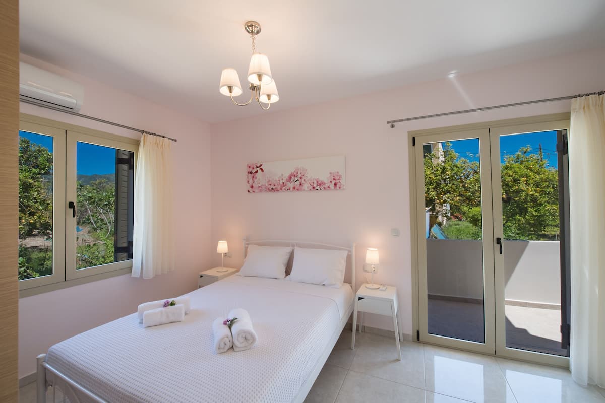 Quarto com cama, duas mesas de cabeceira, um lustre, janela com cortinas e porta de vidro deslizante.