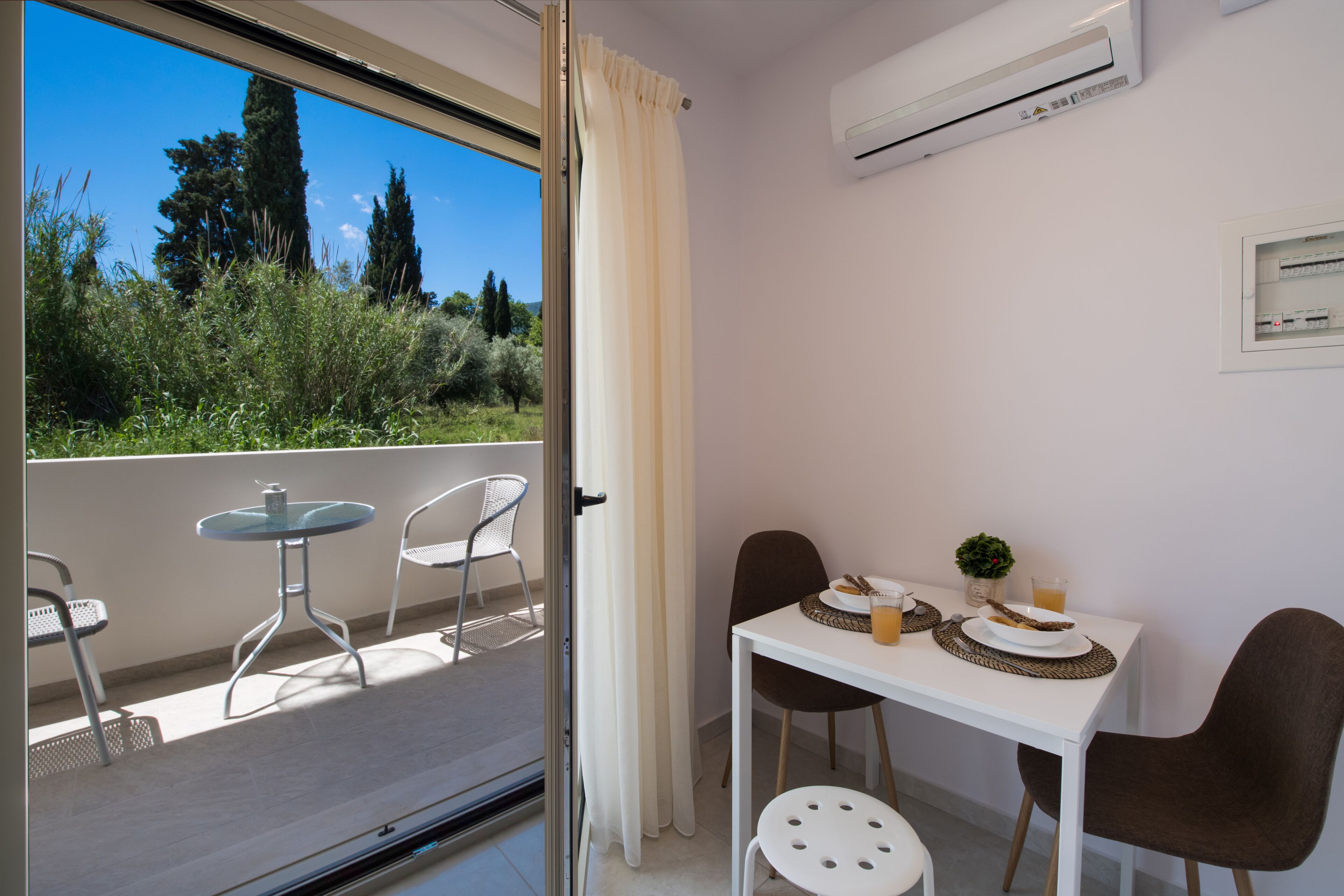 A balcony with a table and chairs, an air conditioning unit, and a view of greenery.