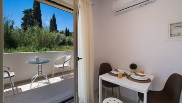 A balcony with a table and chairs, an air conditioning unit, and a view of greenery.