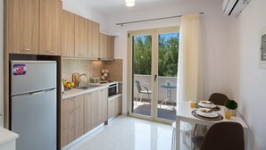 A modern kitchen with wooden cabinets, a refrigerator, a microwave, and a sink. There is a dining area with a table and chairs, and a sliding glass door leading to an outdoor patio. - Bounatsa Studios & Apartments (Lefkada)