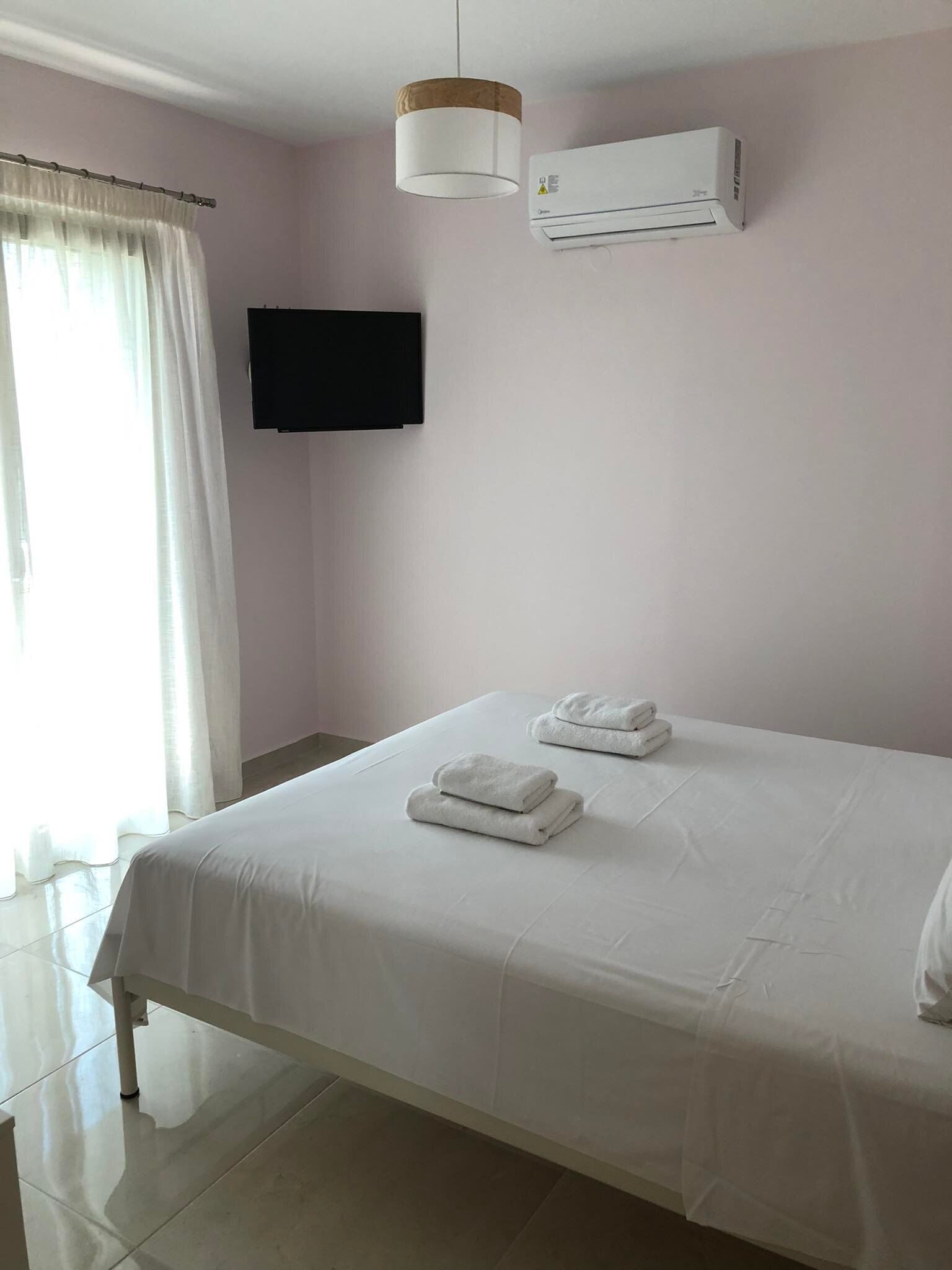 A hotel room with a bed, white towels, an air conditioning unit, a television, and a window with curtains.