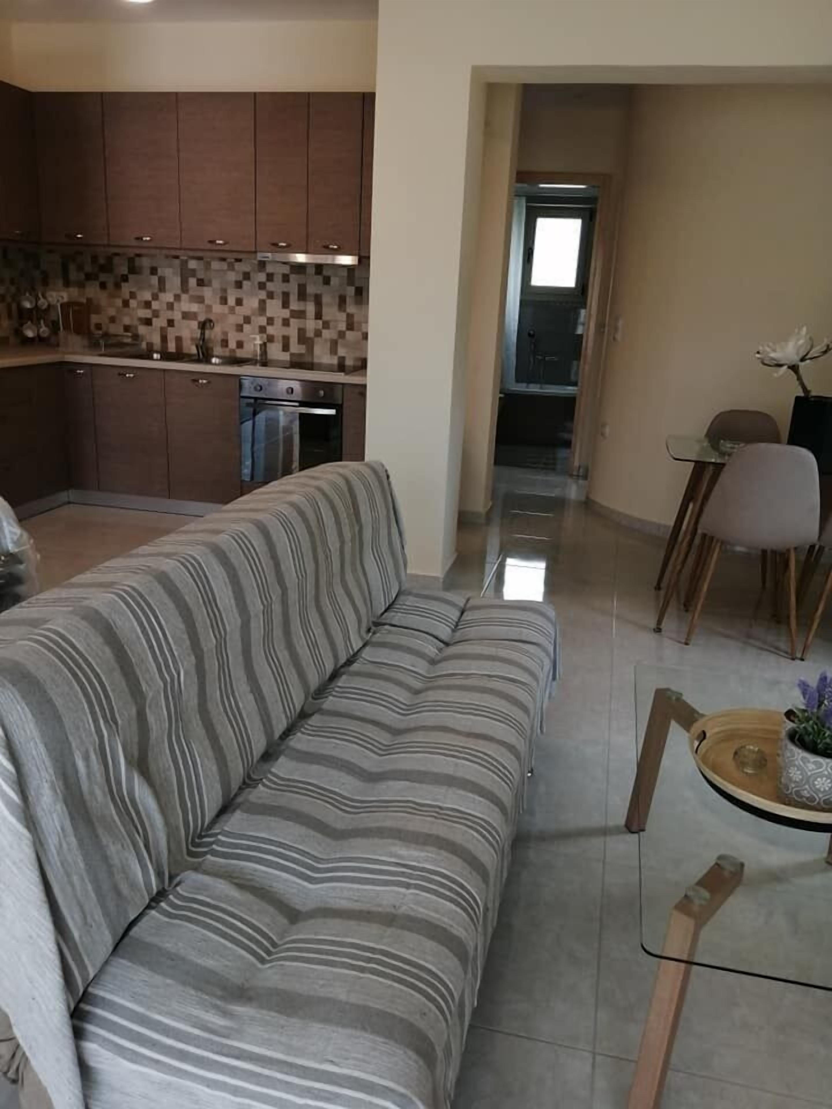 Ein Wohnzimmer mit einem gestreiften Sofa, ein Essbereich mit Tisch und Stühlen sowie eine Küche mit Holzschränken und einer gefliesten Rückwand.