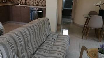 Ein Wohnzimmer mit einem gestreiften Sofa, ein Essbereich mit Tisch und Stühlen sowie eine Küche mit Holzschränken und einer gefliesten Rückwand.