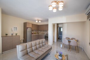 A modern living room with a sofa, a dining area with chairs and a table, a kitchen with cabinets and appliances, and a ceiling with recessed lighting.