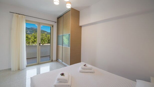 A hotel room with a bed, two towels, a sliding glass door to a balcony, and a ceiling light fixture. - Bounatsa Studios & Apartments (Lefkada)