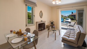 A modern living room with a glass dining table, sofa, fireplace, and a view of the outside. - Bounatsa Studios & Apartments (Lefkada)