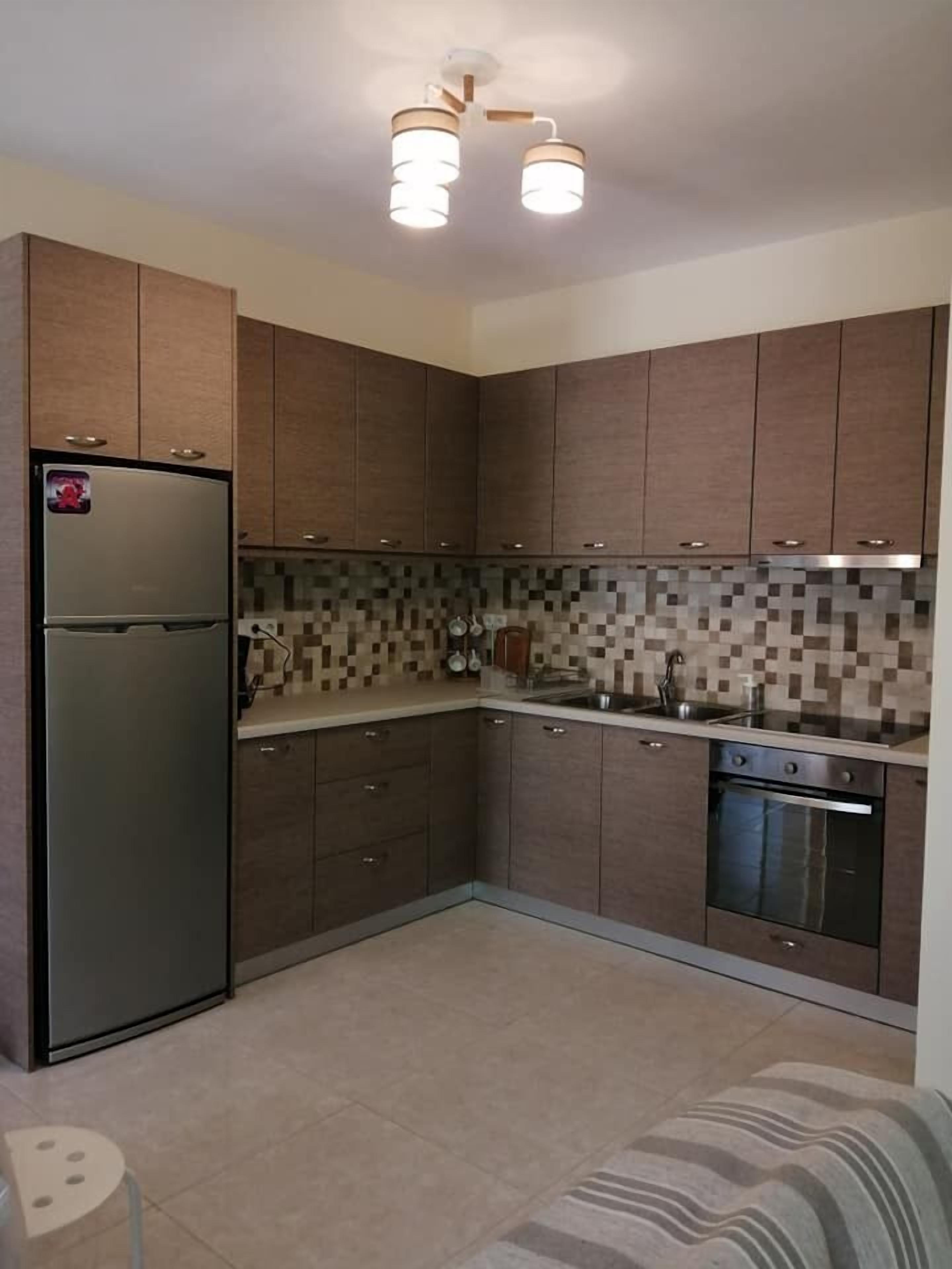 A modern kitchen with dark wooden cabinets, a stainless steel refrigerator, a tiled backsplash, and a built-in oven.