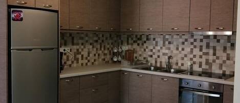 A modern kitchen with dark wooden cabinets, a stainless steel refrigerator, a tiled backsplash, and a built-in oven.