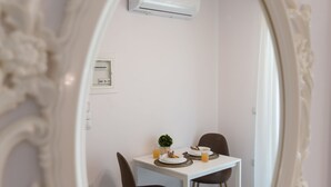 A room with a white ornate mirror reflecting a dining area with a table, chairs, and an air conditioning unit on the wall. - Bounatsa Studios & Apartments (Lefkada)