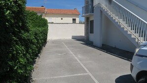 A parking area with a white car, a hedge, and a building with a red-tiled roof. - Sol-y-Days le Goéland, Seafront apartment with parking (Le Grau-du-Roi)