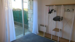 A room with a sliding glass door, a small bed, a wardrobe with hanging items, and a radiator. - Sol-y-Days le Goéland, Seafront apartment with parking (Le Grau-du-Roi)