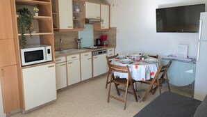 Cozinha compacta com armários de madeira, micro-ondas, pia e mesa de jantar para quatro pessoas.