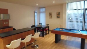 Un salon moderne doté d’une table de billard, d’un coin bar avec des tabourets, d’une table à manger avec des chaises et de grandes fenêtres.