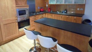 Une cuisine avec des meubles de rangement en bois, une cuisinière, un four à micro-ondes et deux tabourets de bar.