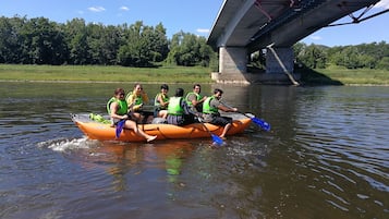 A group of people on a small orange raft with life jackets, paddling under a bridge.