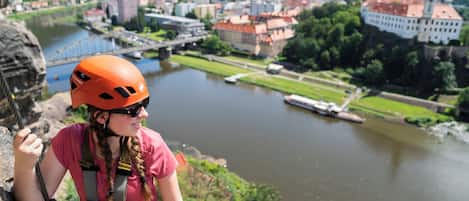 Una persona escala una roca con vistas a un río y edificios al fondo.