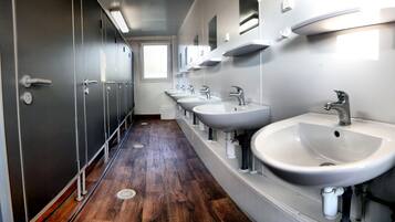 A row of sinks with mirrors above them, wooden flooring, and a window at the end of the hallway.