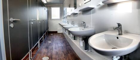 A row of sinks with mirrors above them, wooden flooring, and a window at the end of the hallway.