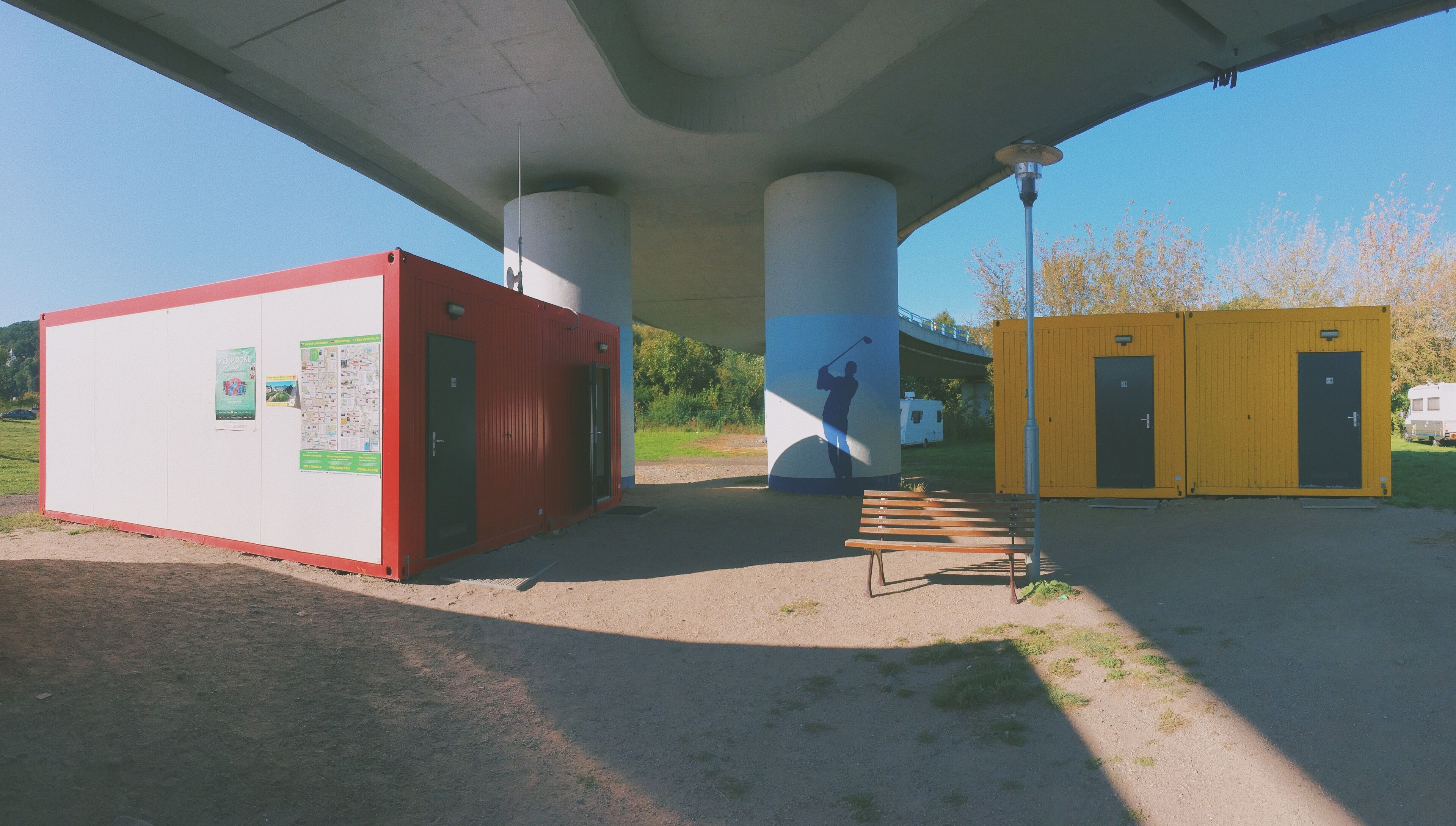 Un espacio al aire libre cubierto con un edificio rojo y amarillo, una banca y un cartel en el edificio rojo.