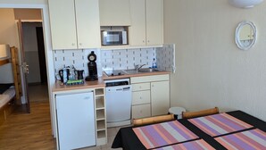 A compact kitchen with a microwave, coffee maker, and dishwasher, a small refrigerator, and a dining area with a striped tablecloth.