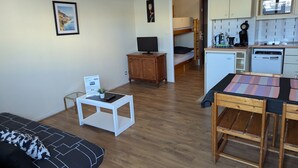 A compact living space with a sofa, a small table, a television, a bunk bed, and a kitchenette.