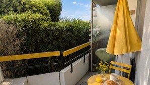 A balcony with a yellow table, chairs, a small vase with flowers, a cup, and a glass of orange juice.