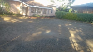 Um edifício com telhado plano, um pequeno jardim frontal e uma área pavimentada na frente.
