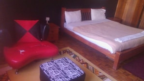 Quarto com cama, mesa de cabeceira, cadeira vermelha e um banquinho estampado.