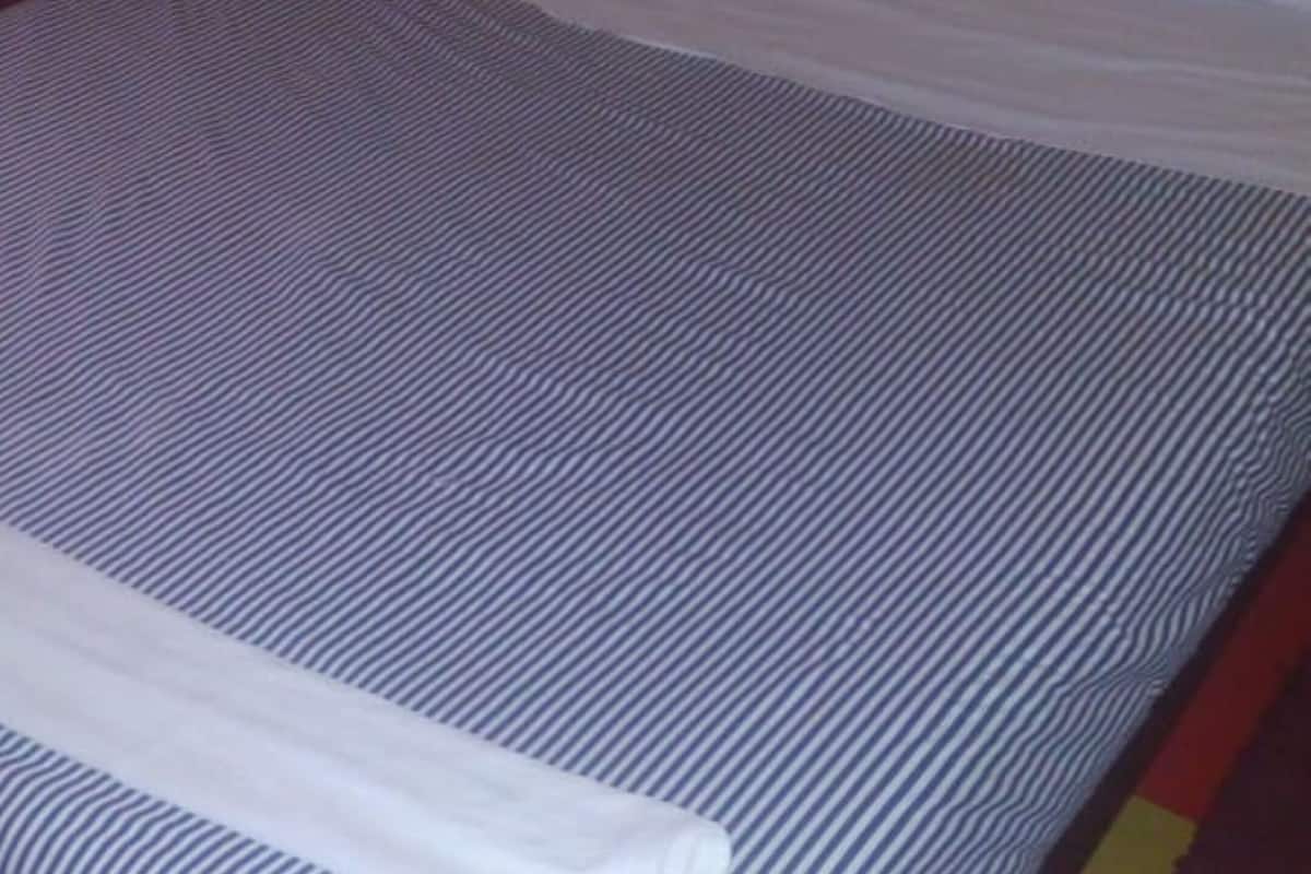 A bed with a striped bedspread and white pillows, set against a yellow wall.