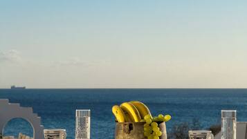 Ett bord med en fruktskål som innehåller bananer och druvor, två glas och ett fartyg i fjärran.