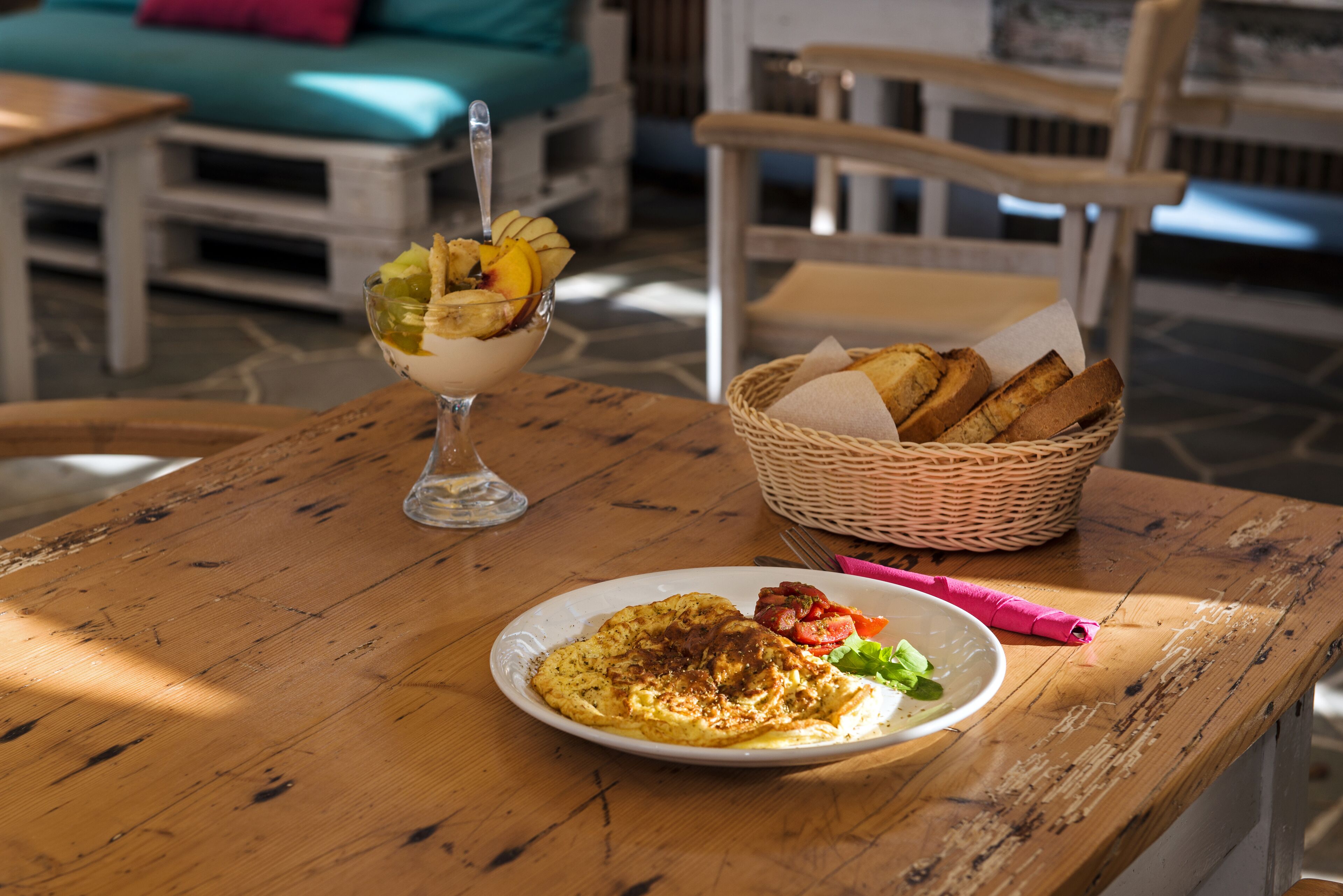 Una mesa de madera con un plato de comida, un vaso de bebida y una cesta de pan.