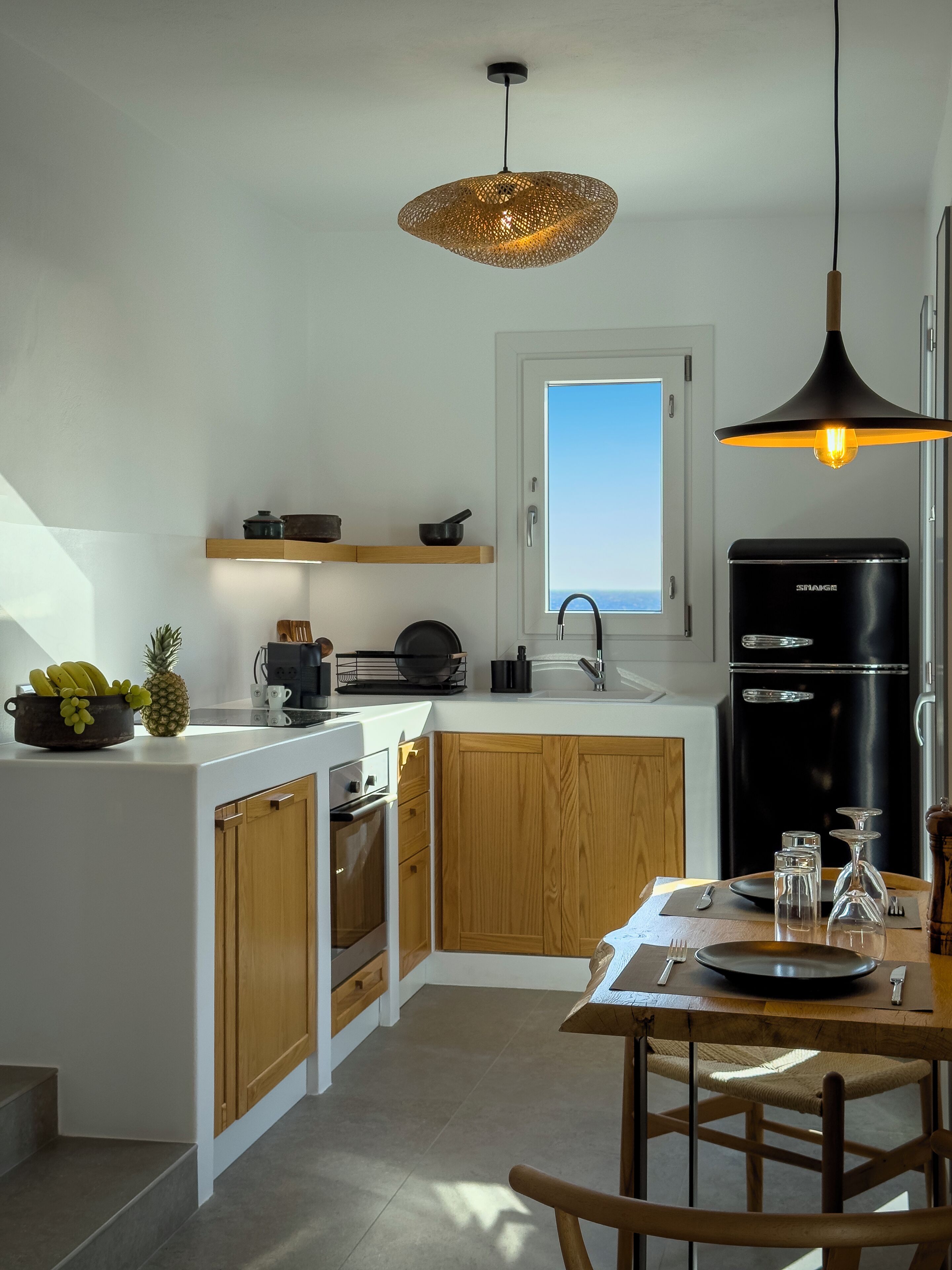 A modern kitchen with wooden cabinets, a black refrigerator, and a hanging light fixture.