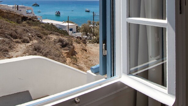 A window with a view of the sea, a white building, and a clear sky.