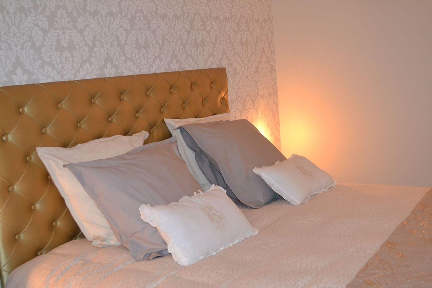 A bed with a tufted headboard, multiple pillows, and a textured wall.