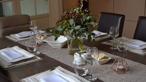 Una mesa de comedor lista para una comida, con platos, vasos y un jarrón de flores.