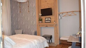Un dormitorio con cama, televisor montado en una pared de madera, una mesita pequeña y una lámpara colgante.