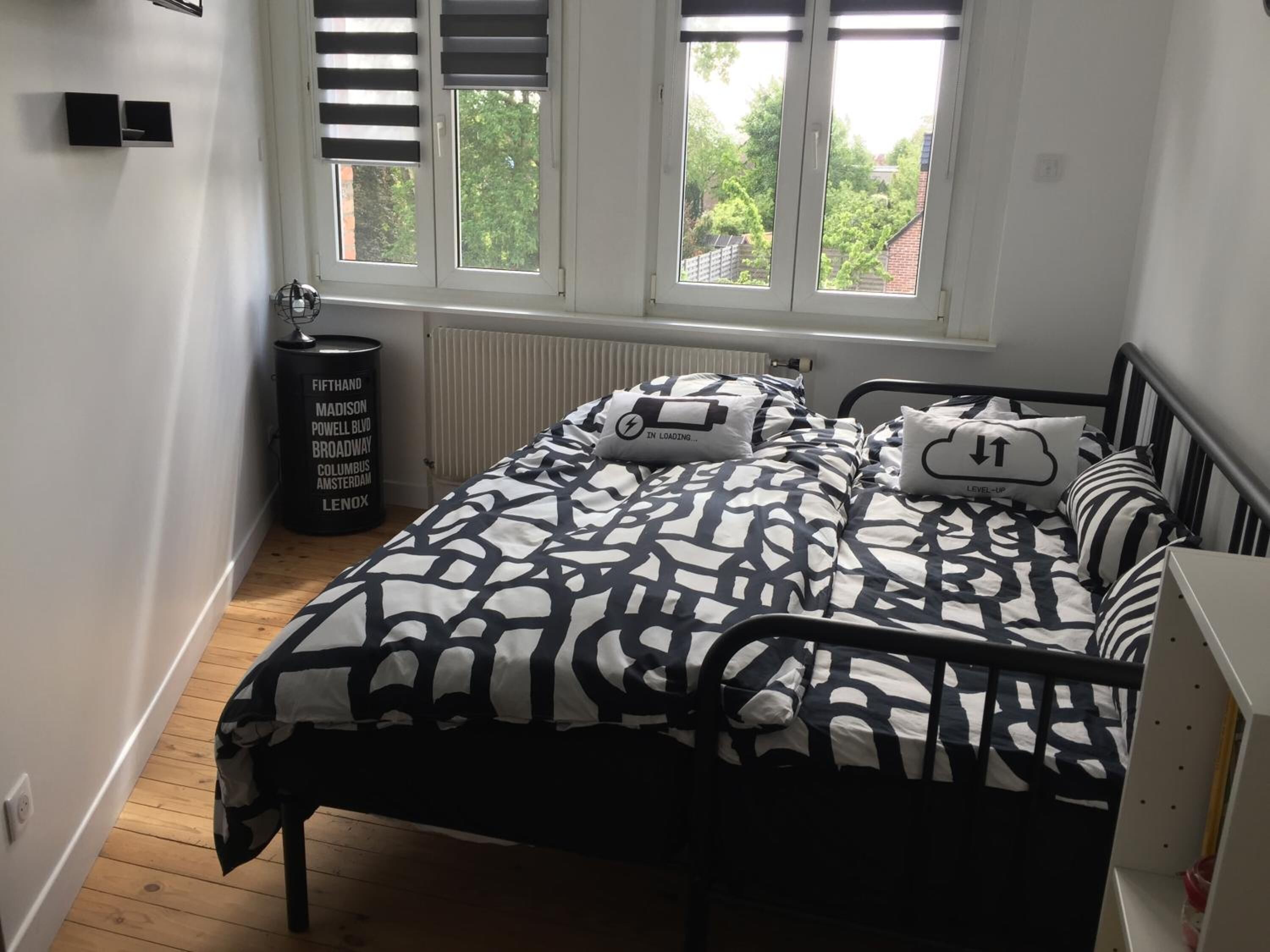Ein Schlafzimmer mit einem Bett, einem Heizkörper, einem Fenster und einer schwarzen Mülltonne.