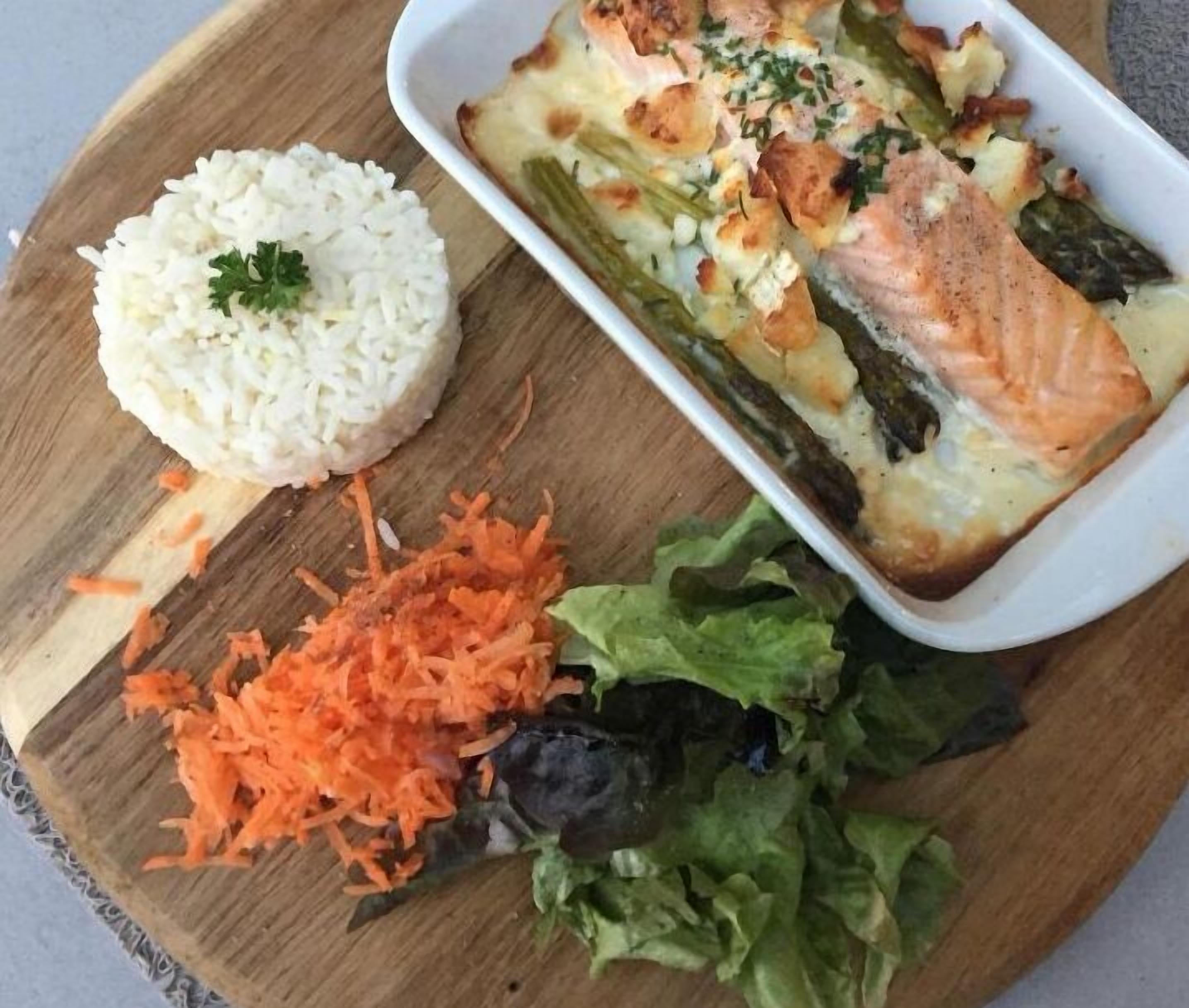 A meal consisting of rice, salmon, asparagus, and shredded carrots on a wooden board.