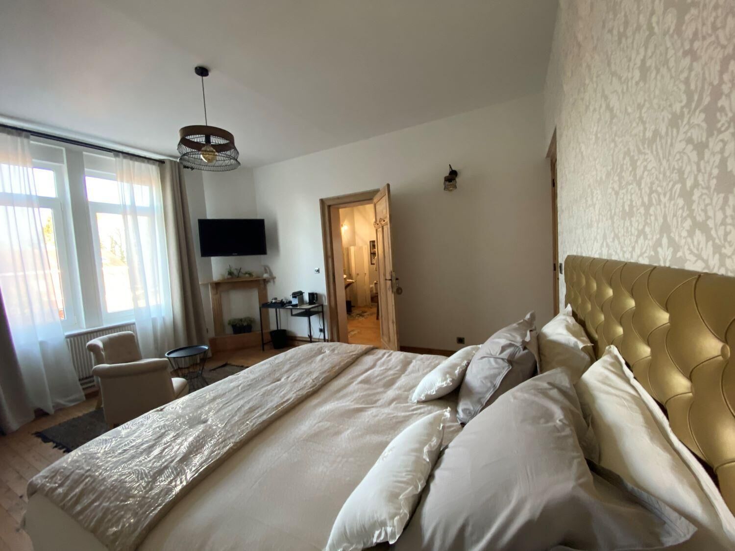 A hotel room with a large bed, a television mounted on the wall, a desk with a chair, and a fireplace.