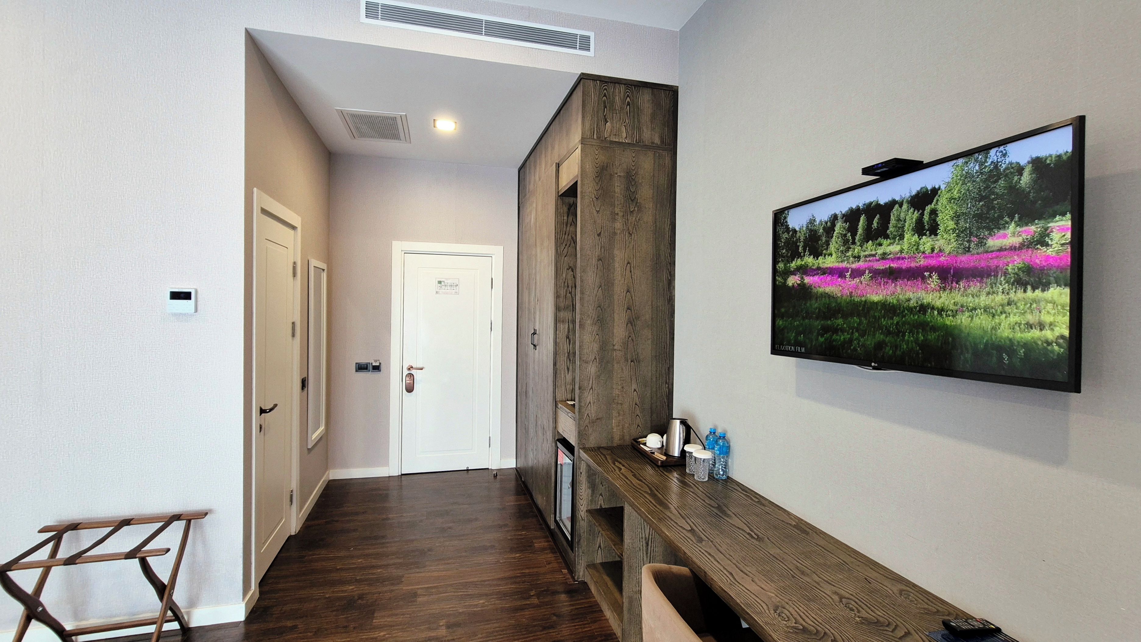A hallway with a wooden bench, a mounted television displaying a nature scene, and a door at the end.
