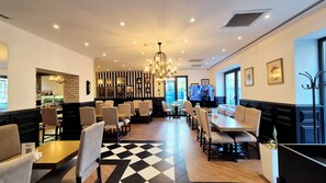 A restaurant with a black and white checkered floor, multiple tables and chairs, a chandelier, and a television screen. - Port Rivoli Baku Hotel (Baku)