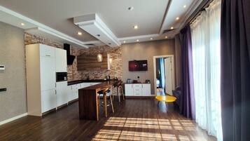 A modern kitchen with a bar area, a dining table, and a television mounted on the wall.