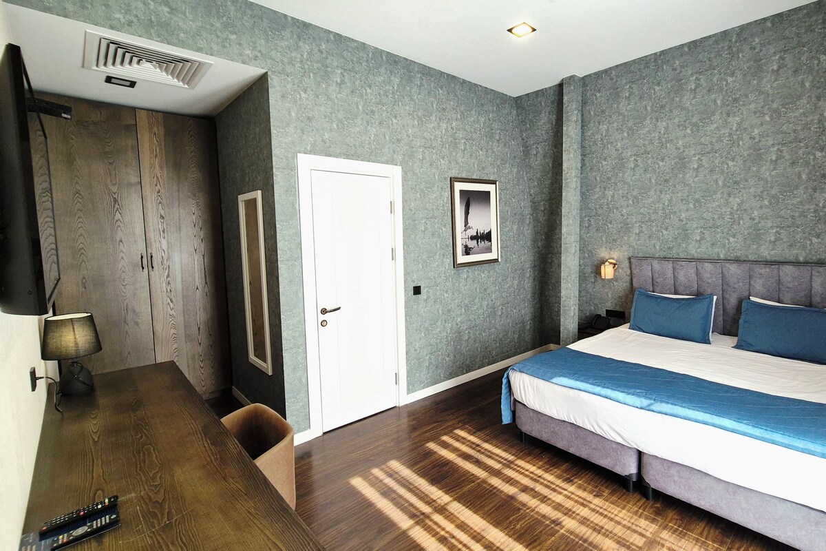A bedroom with a bed, a nightstand, a lamp, a wardrobe, and a door.