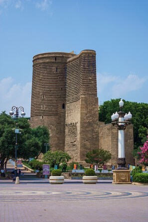 A historic tower with a circular base and a rectangular upper section, surrounded by a landscaped area with benches and decorative elements. - Port Rivoli Baku Hotel (Baku)