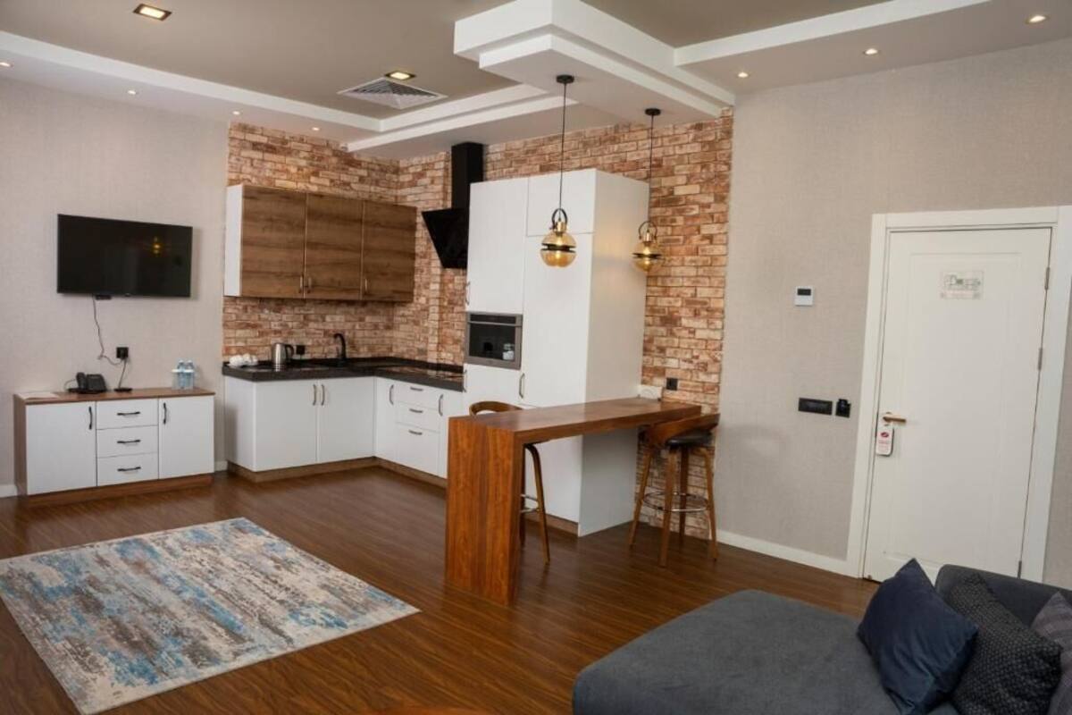Cocina moderna con armarios blancos, pared de ladrillo decorativa y comedor con mesa de madera y taburetes de bar.