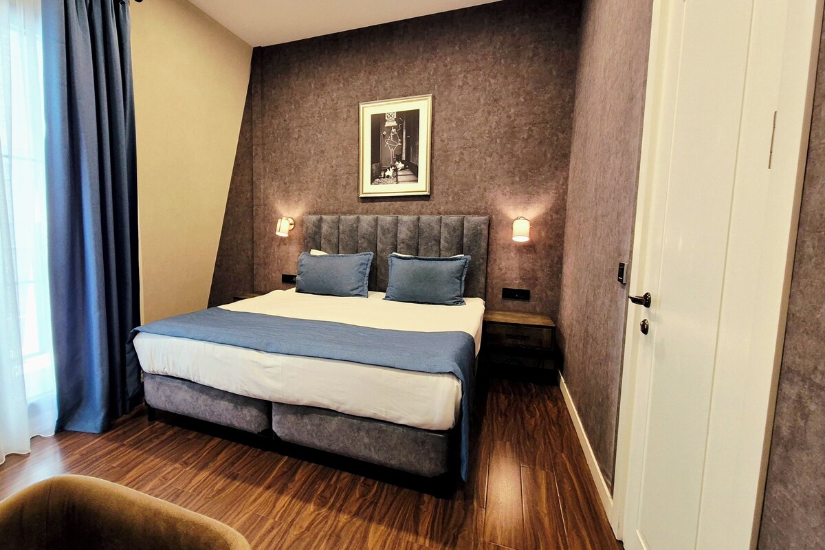 A modern hotel room with a large bed, a nightstand, a wall-mounted picture, and a door.